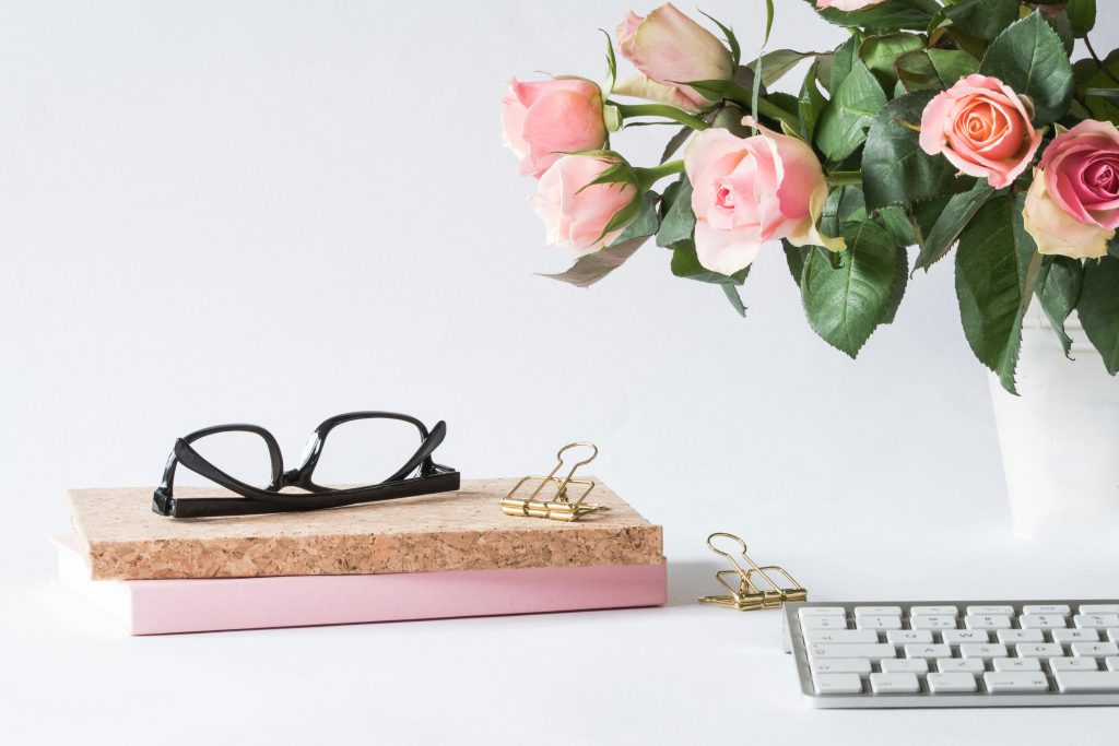Stylish workspace featuring pink roses, glasses, keyboard, and notebooks. Perfect for spring office decor.
